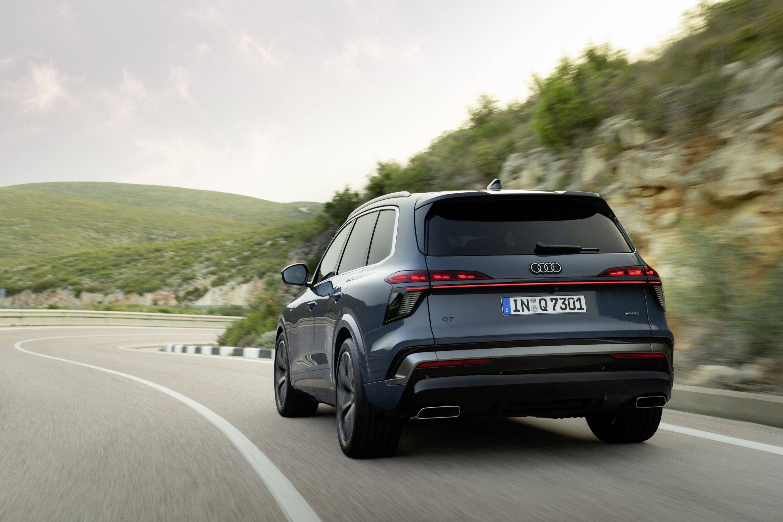 A traseira do Audi Q7 de 3.ª geração em azul Alopias, em andamento, numa fotografia oficial da Audi.