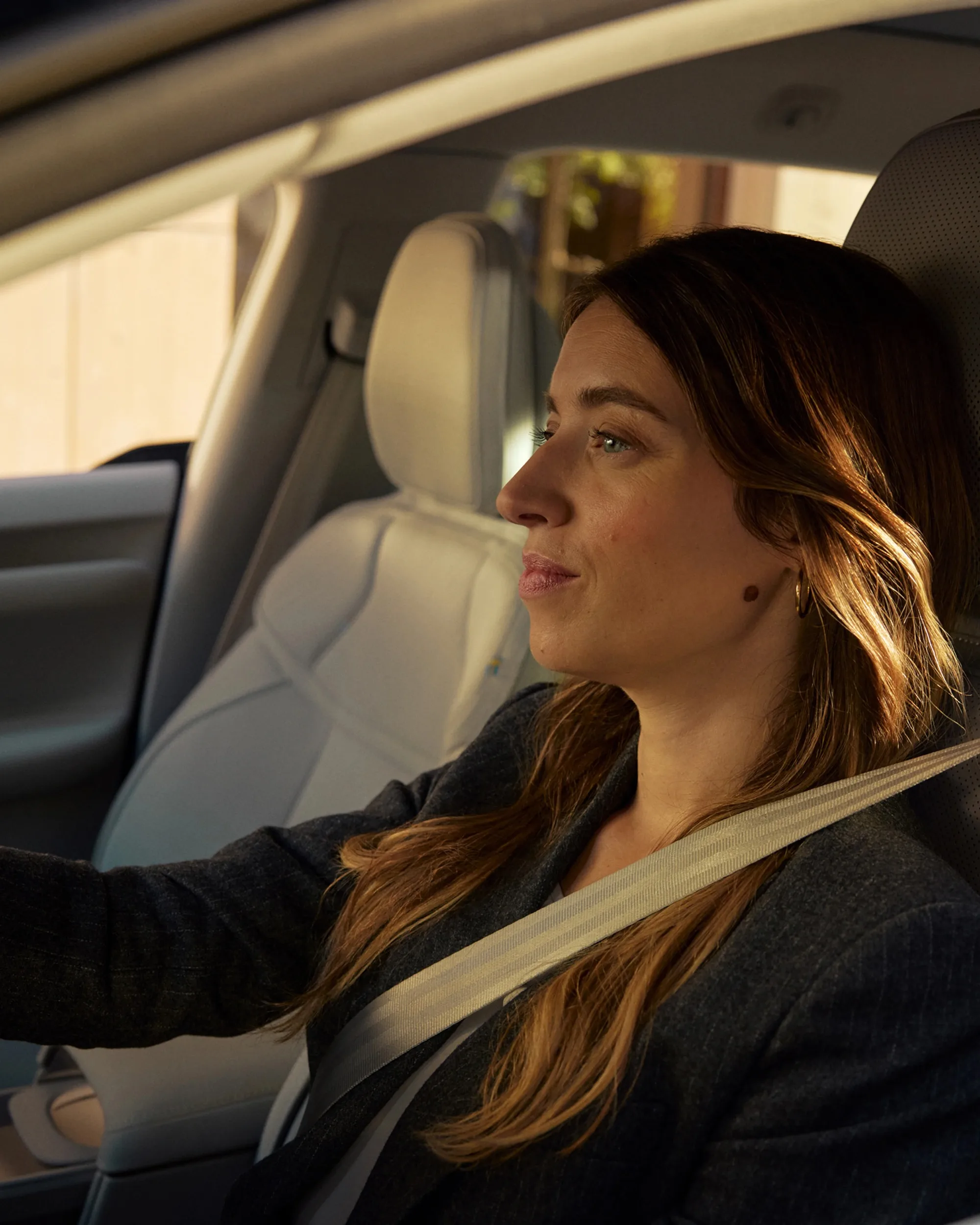 A driver sits inside the Volvo EX60 with a seatbelt fastened, looking ahead.